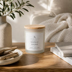 A frosted glass jar candle with a light wood lid sits on a wooden table. The label reads 'Nordic Shore' by 'Ardent North'.