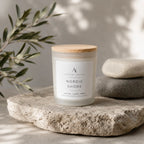 A frosted glass jar candle with a light wood lid sits on a rough stone slab. The label reads 'Nordic Shore' by 'Ardent North'.
